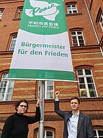 Bürgermeister Nico Ruhle und seine Stellvertreterin Daniela Kuzu vor der Mayors for Peace-Flagge am Rathaus Neuruppin